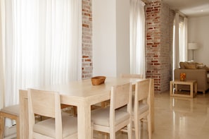 A dining area with a wooden table and chairs, a basket on the table, and a brick wall in the background.