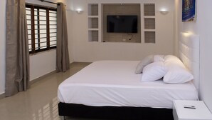 A modern bedroom with a large bed, a flat-screen TV mounted on the wall, and a bedside table with a lamp.