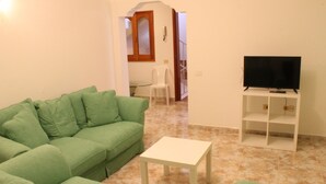 A living room with a green sofa, a white table, and a TV on a stand. - Mele Sky Beach, 1, sea views, terrace and sun (Lomo Quiebre)
