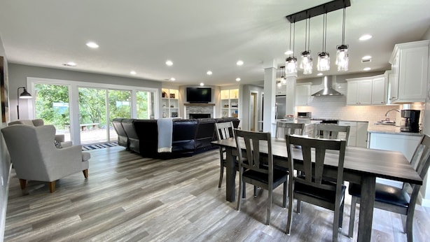 A modern kitchen with white cabinets, a dining area with a wooden table and chairs, and a living area with a black sofa and a fireplace. - Gorgeous Mountain View,  6 Private acres, Close to Downtown! (Hot Springs)