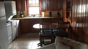 A cozy cabin interior with wooden walls, a kitchenette, a dining area with a table and chairs, and a striped sofa with a pillow. - The Pirates' 2 Bedroom Cottage by RedAwning (Kitty Hawk)