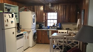 A compact kitchen with wooden cabinets, a washing machine, a refrigerator, and a dining area with a table and chairs. - The Pirates' 2 Bedroom Cottage by RedAwning (Kitty Hawk)