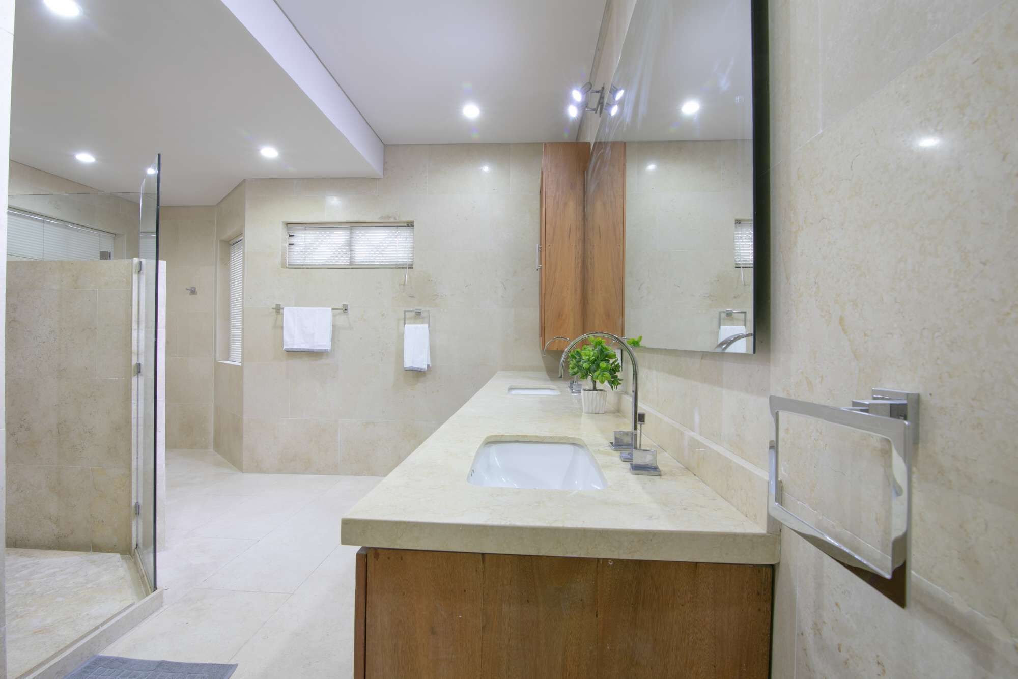 A modern bathroom with a large mirror, two sinks, and a shower area.