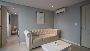 Un salon moderne avec un canapé beige, une table basse blanche et une œuvre d’art encadrée accrochée au mur.