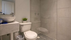 Une salle de bain avec un lavabo, des toilettes et une douche, le tout de couleur blanche.