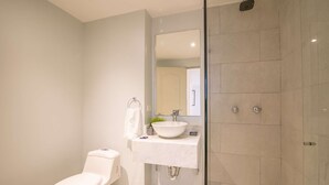 A modern bathroom with a toilet, sink, and glass shower enclosure. - Brand New 1 BR Apartment in Bocagrande (Cartagena)