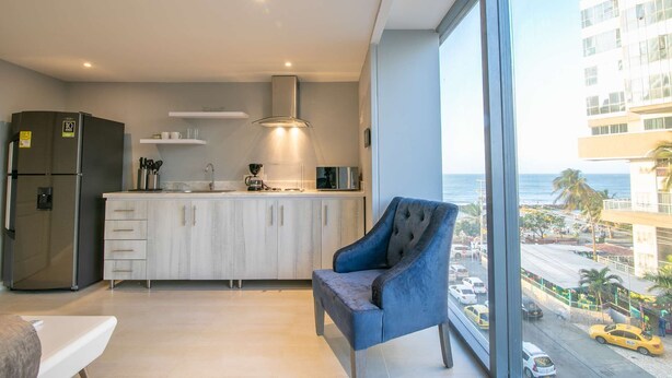 A modern kitchen with a large island, a built-in oven, and a view of the ocean through large windows. - Brand New 1 BR Apartment in Bocagrande (Cartagena)