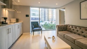 A modern living room with a sofa, a dining table, and a kitchen area with a microwave and coffee maker. - Brand New 1 BR Apartment in Bocagrande (Cartagena)