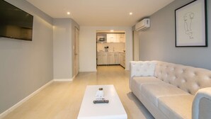 A modern living room with a white sofa, a white coffee table with a remote control, and a framed artwork on the wall.