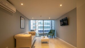 A modern living room with a sofa, a coffee table, and a chair. There is a large window with a view of buildings outside. - 1 Bedroom Stunning Apartment in Bocagrande (Cartagena)