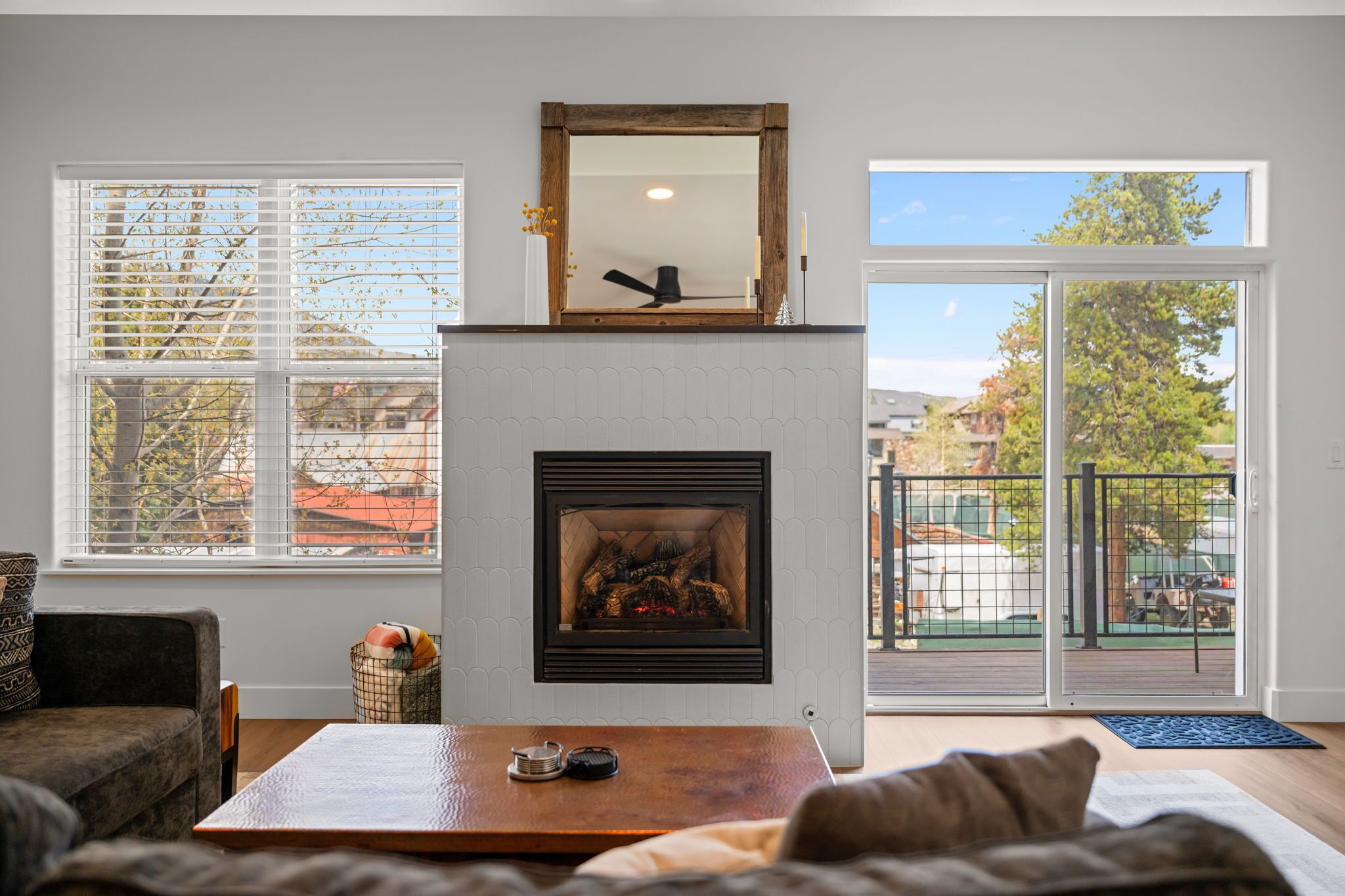 Ein Wohnzimmer mit Kamin, einer Couch, einem Couchtisch und Blick ins Freie durch große Fenster.