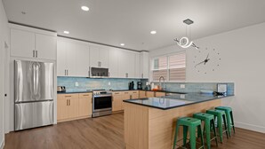 A modern kitchen with white cabinets, stainless steel appliances, a central island with stools, and a clock on the wall.
