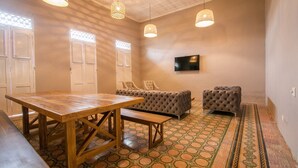 A room with a wooden table, two tufted sofas, a TV on the wall, and patterned flooring.