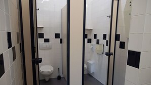 Een toiletruimte met witte betegelde muren, zwart-wit geruite tegels, een wit toilet, een zwarte vloerwisser en een handdroger.
