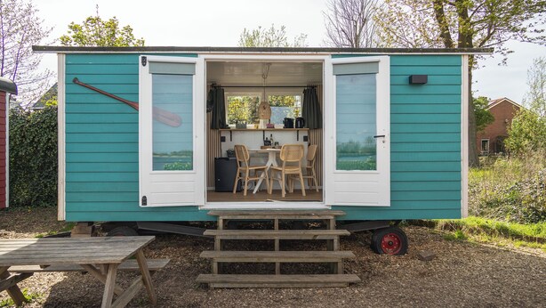 Een kleine, verplaatsbare woonwagen met een keukenhoek, eettafel en stoelen.