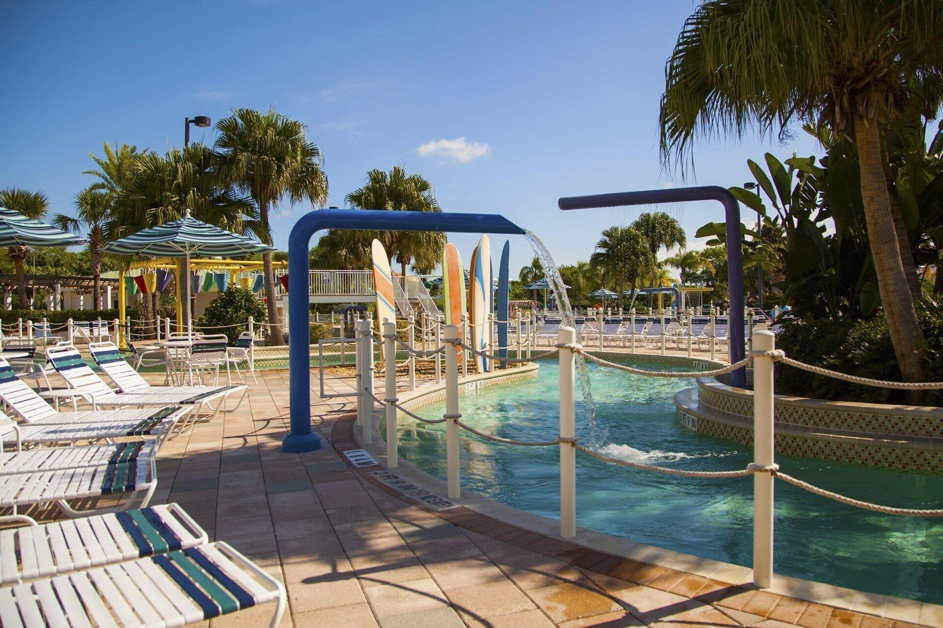 A pool area with lounge chairs, palm trees, and a water feature.