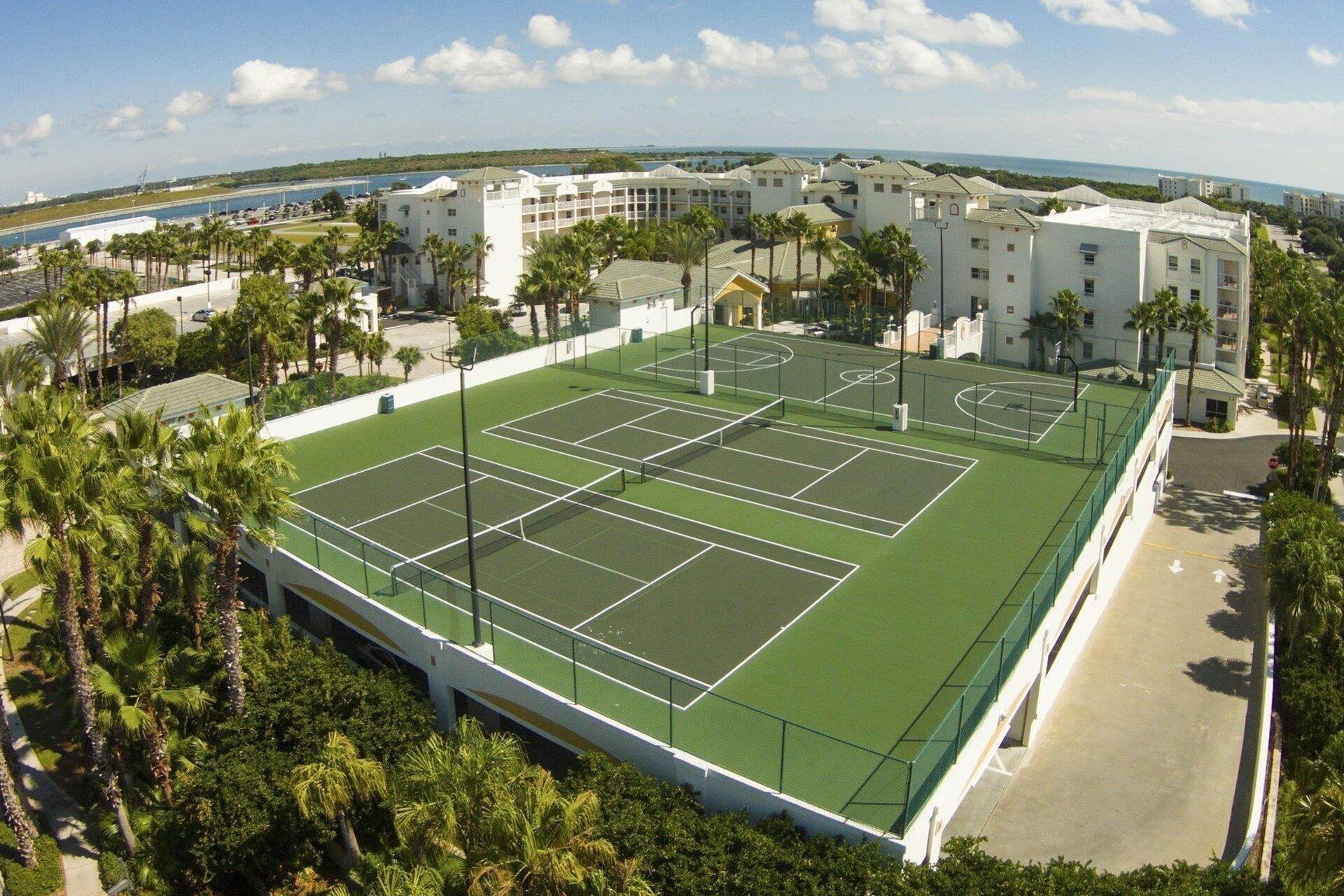 Vista aérea de una cancha de tenis rodeada de palmeras y edificios.
