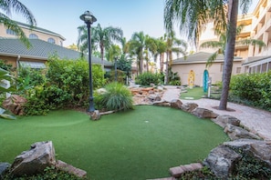 A courtyard with artificial grass, palm trees, and a pathway.