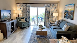 A living room with a television, sofa, armchair, coffee table, and a view to the outside.