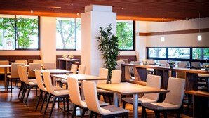 A modern dining area with wooden tables and chairs, large windows, and a central plant. - Inn Juraku Formerly Spa Riraku (Toon)
