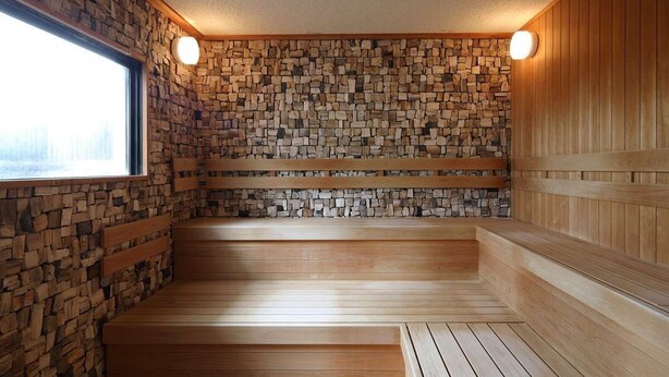 A sauna with wooden benches and a stone wall. - Inn Juraku Formerly Spa Riraku (Toon)