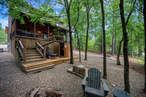 Eine Hütte mit einer Holzdielen-Terrasse, Sitzgelegenheiten im Freien und einem Wald im Hintergrund.