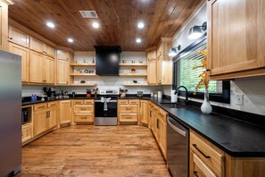 A modern kitchen with wooden cabinets, stainless steel appliances, and a black countertop. - Modern 1BR Hot Tub Retreat with Pool Table (Broken Bow)