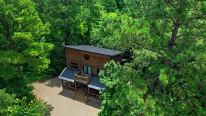 Eine moderne Holzhütte, umgeben von dichtem Wald, mit einer Terrasse und einem großen Fenster.