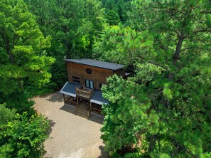Eine moderne Holzhütte, umgeben von dichtem Wald, mit einer Terrasse und einem großen Fenster.