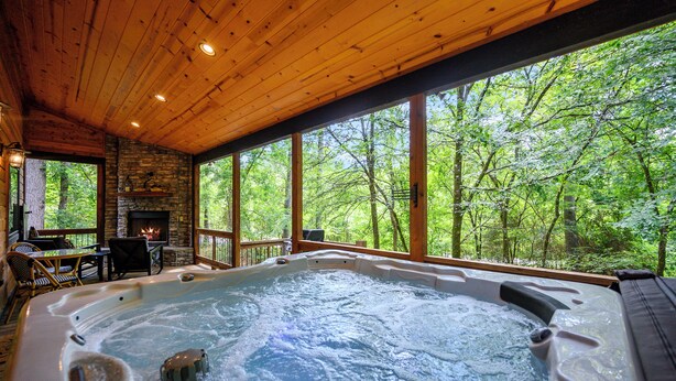 Ein Whirlpool mit Kamin aus Stein, einer Holzterrasse und Blick auf einen Wald.