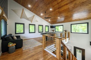 A spacious room with a wooden ceiling, a black sofa, a pool table, and a staircase. - Modern 1BR Hot Tub Retreat with Pool Table (Broken Bow)