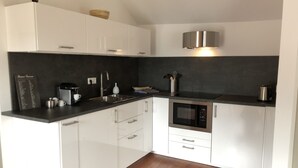 A modern kitchen with white cabinets, a black countertop, a built-in oven, and a stainless steel kettle.