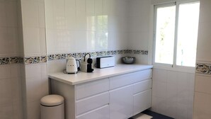 Une petite cuisine avec des meubles blancs, un plan de travail blanc, un grille-pain, une bouilloire et un saladier.