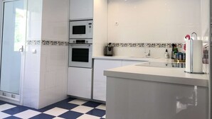 Une cuisine moderne avec des meubles blancs, un four encastré, un four à micro-ondes et un évier.