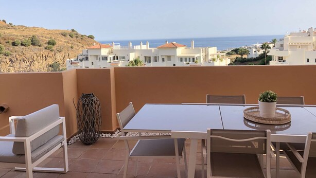 Une terrasse avec une table et des chaises, un pot de fleurs et une vue sur la mer et les bâtiments.