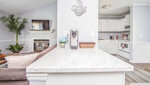A modern kitchen with white cabinetry, a marble island, and a coffee-themed wall decal. - Cozy 2BR Quadraplex Minutes to Ft Bragg w/ Deck (Fayetteville)