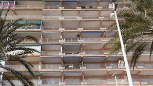 Un immeuble résidentiel à plusieurs étages, doté de balcons, d’un lampadaire et de palmiers.