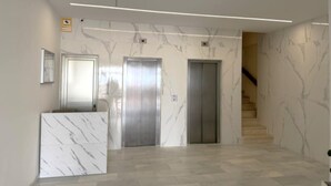 Un hall d’entrée moderne avec des murs en marbre, deux ascenseurs, un comptoir d’accueil et un escalier.