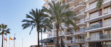 A multi-story hotel with balconies, palm trees, and flags.