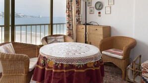 Un balcon agrémenté de meubles en osier, une table ronde recouverte d’une nappe en dentelle et une vue sur la mer.