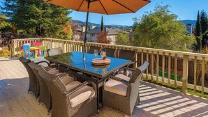 A deck with wicker furniture, a glass-top table, and an umbrella. - The Solterra | Wine Country 5BR, Views, EV, Games (Santa Rosa)