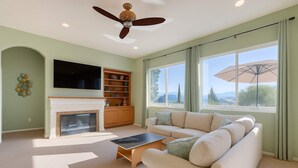 A spacious living room with a fireplace, a flat-screen TV, a sofa, and a ceiling fan. - The Solterra | Wine Country 5BR, Views, EV, Games (Santa Rosa)
