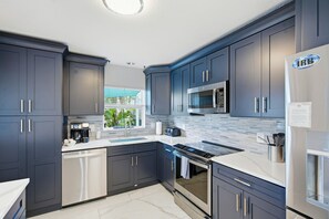 A modern kitchen with dark cabinets, stainless steel appliances, and a tiled backsplash. - 80’s Paradise golf cart, rooftop deck heated pool (Indian Rocks Beach)