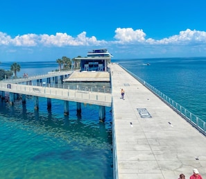 A pier extending into a clear blue sea with a modern building at the end. - 80’s Paradise golf cart, rooftop deck heated pool (Indian Rocks Beach)