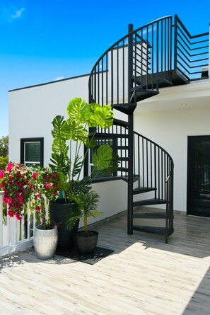 A modern building with a spiral staircase leading to an upper level. There are potted plants and flowers in the foreground. - 80’s Paradise golf cart, rooftop deck heated pool (Indian Rocks Beach)