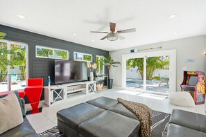 A modern living room with a flat-screen TV, red and black sofas, a ceiling fan, and a view of the outdoors. - 80’s Paradise golf cart, rooftop deck heated pool (Indian Rocks Beach)
