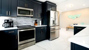 A modern kitchen with dark cabinetry, stainless steel appliances, and a marble countertop.