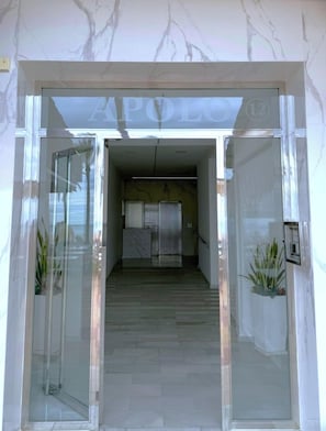 A hotel entrance with a marble facade, a glass door, and a hallway leading to a reception area.
