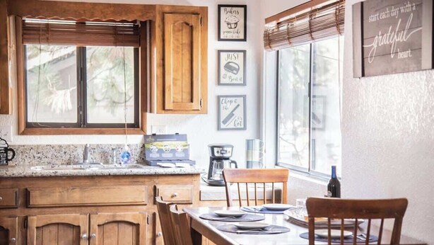 Una cocina con armarios de madera, encimera de granito y una mesa de comedor con sillas. En la pared hay citas inspiradoras enmarcadas.