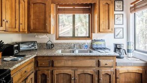 Una cocina con armarios de madera, encimera de granito, ventana con persianas y diversos electrodomésticos.